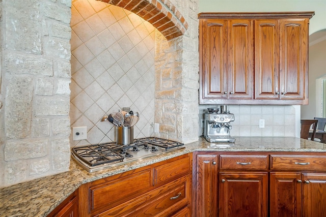 kitchen with stainless steel gas cooktop, brown cabinets, light stone counters, and decorative backsplash