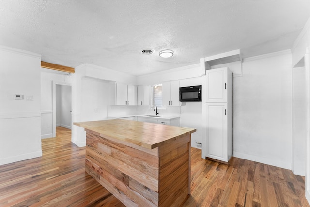 1909 Sycamore Dr, Mesquite, TX 75149 - kitchen with black microwave, wooden counters, a sink, a textured ceiling, and light wood-style flooring
