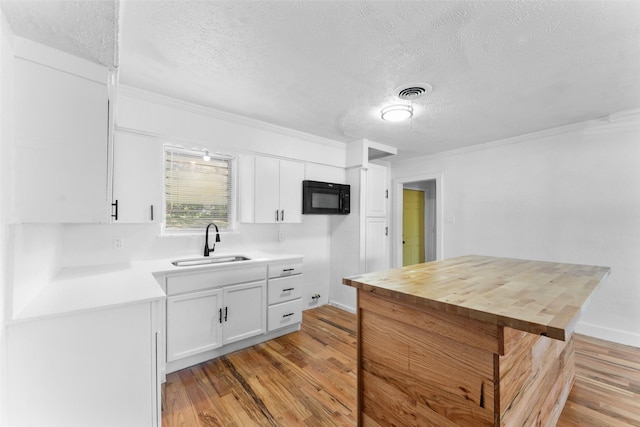 1909 Sycamore Dr, Mesquite, TX 75149 - kitchen with a sink, black microwave, a textured ceiling, light wood-type flooring, and white cabinetry