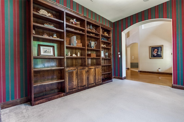 carpeted empty room featuring arched walkways, wallpapered walls, and baseboards