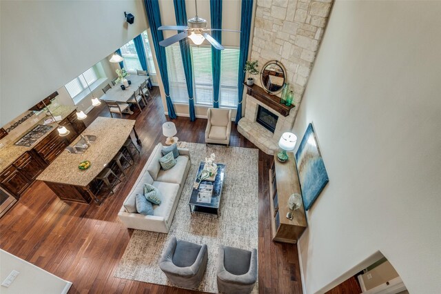 living room featuring ceiling fan, a stone fireplace, wood finished floors, and a high ceiling