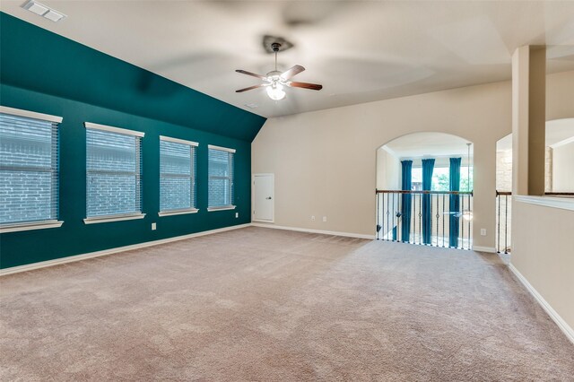 carpeted empty room featuring ceiling fan, arched walkways, baseboards, lofted ceiling, and visible vents
