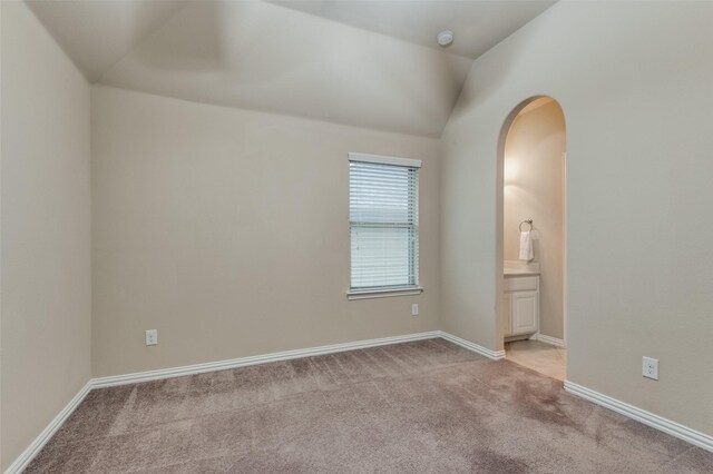 unfurnished bedroom with baseboards, ensuite bathroom, carpet flooring, and arched walkways