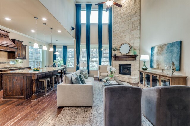 living room featuring a ceiling fan, a fireplace, ornamental molding, a high ceiling, and dark wood-type flooring
