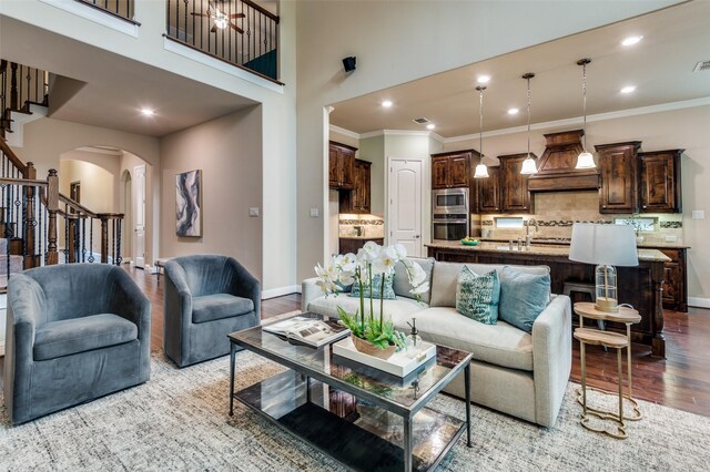living area featuring ornamental molding, stairs, wood finished floors, baseboards, and arched walkways