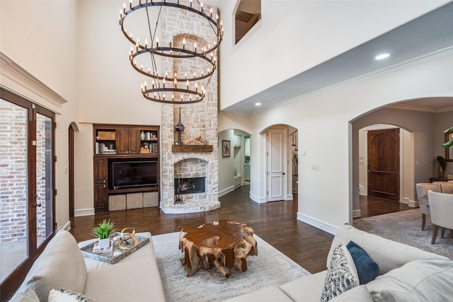 2890 Creekwood Ln, Prosper, TX 75078 - living area featuring arched walkways, a stone fireplace, wood finished floors, a high ceiling, and a chandelier