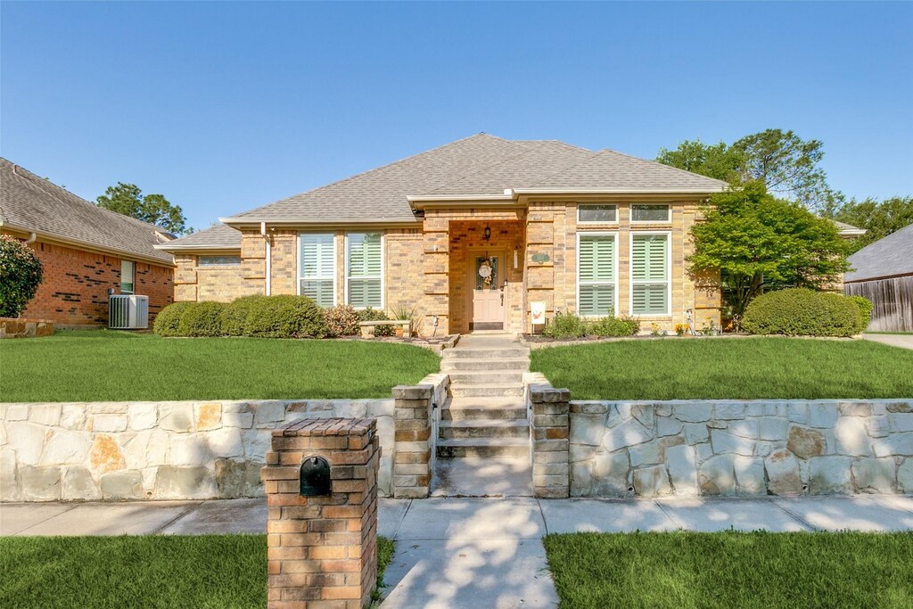 view of front of home featuring a front yard, brick siding, cooling unit, and a shingled roof