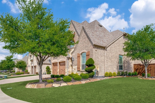 view of front of house featuring a garage, fence, brick siding, a front lawn, and driveway