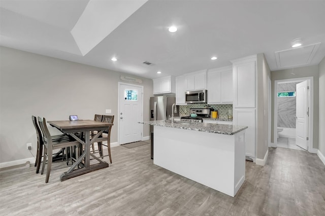 530 E Day St, Denison, TX 75021 - kitchen with an island with sink, light wood-style flooring, white cabinets, stainless steel appliances, and backsplash