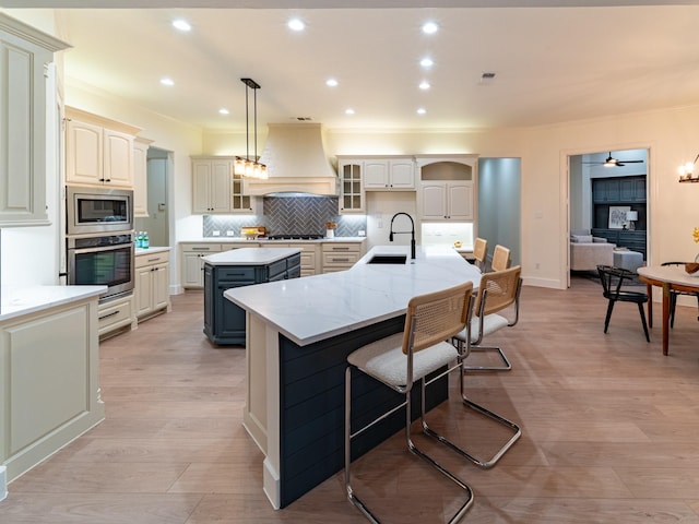 5454 Pebble Creek Dr, Celina, TX 75078 - kitchen with an island with sink, custom exhaust hood, appliances with stainless steel finishes, a sink, and light wood finished floors