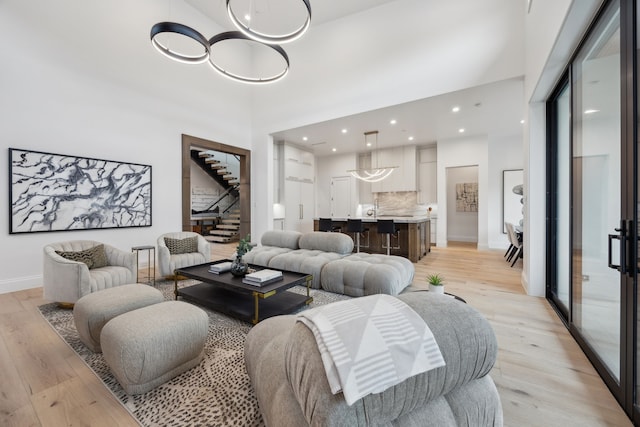 living room featuring light wood-type flooring, baseboards, a high ceiling, and stairs