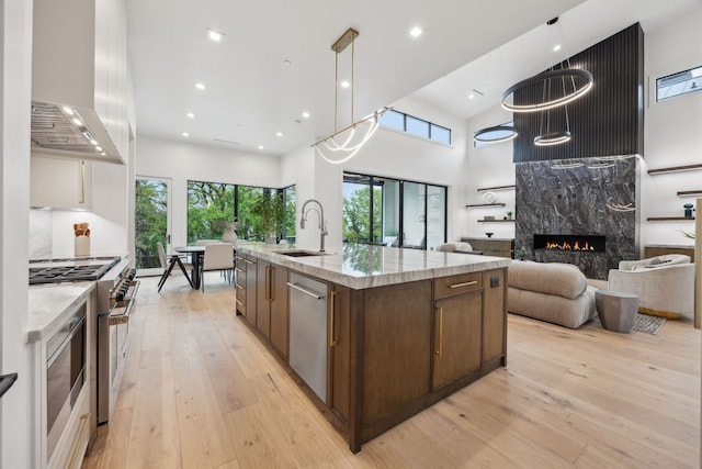 kitchen featuring a high ceiling, a sink, stainless steel appliances, open floor plan, and light wood-style floors