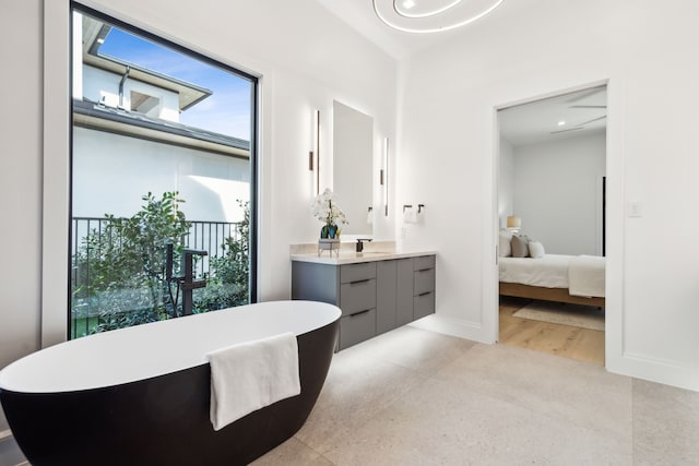 ensuite bathroom featuring vanity, ensuite bath, speckled floor, a soaking tub, and baseboards