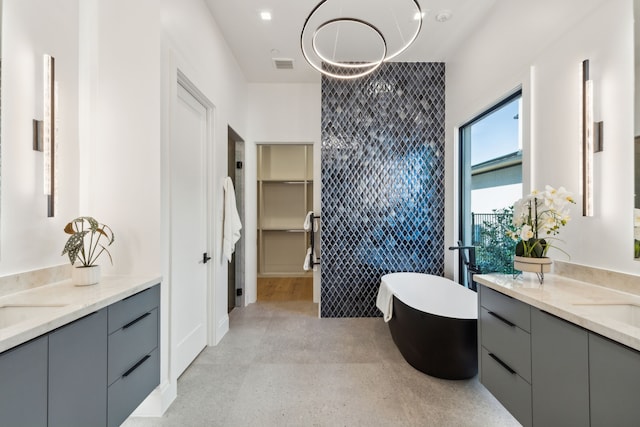 full bath with a sink, two vanities, tile walls, a freestanding bath, and visible vents