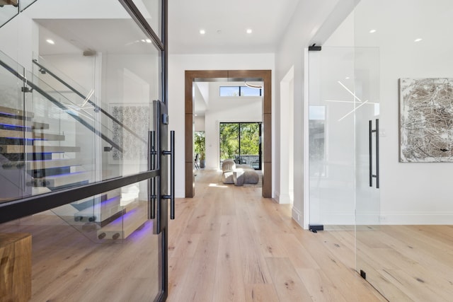 hall with a towering ceiling, baseboards, light wood-type flooring, and recessed lighting