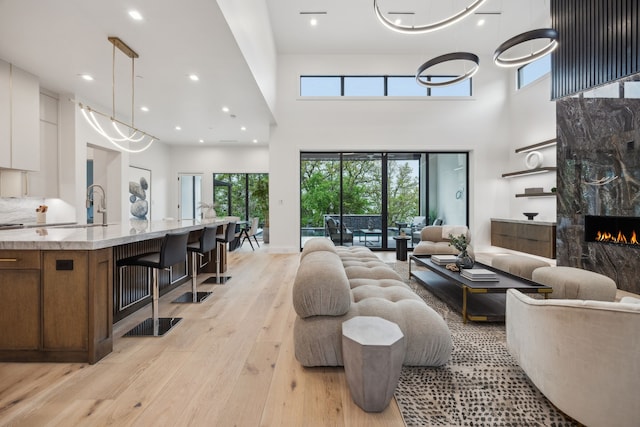 living room featuring a premium fireplace, recessed lighting, light wood-type flooring, and a high ceiling