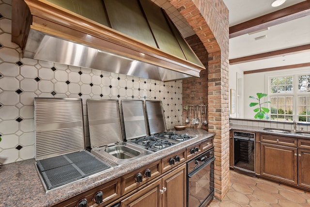 kitchen featuring tasteful backsplash, light tile patterned floors, a sink, wall chimney range hood, and beamed ceiling