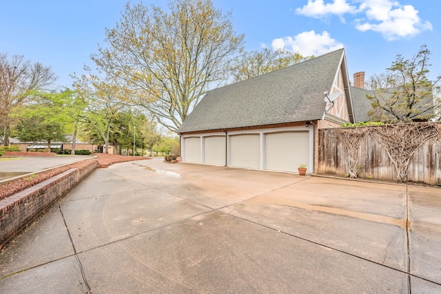 view of side of property featuring a garage, a chimney, fence, concrete driveway, and roof with shingles