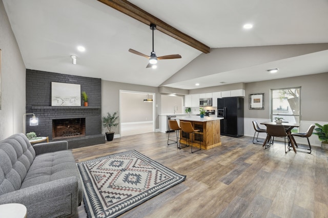 living room featuring ceiling fan, a fireplace, wood finished floors, vaulted ceiling with beams, and baseboards