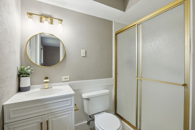 bathroom featuring a shower with shower door, vanity, toilet, and a textured wall