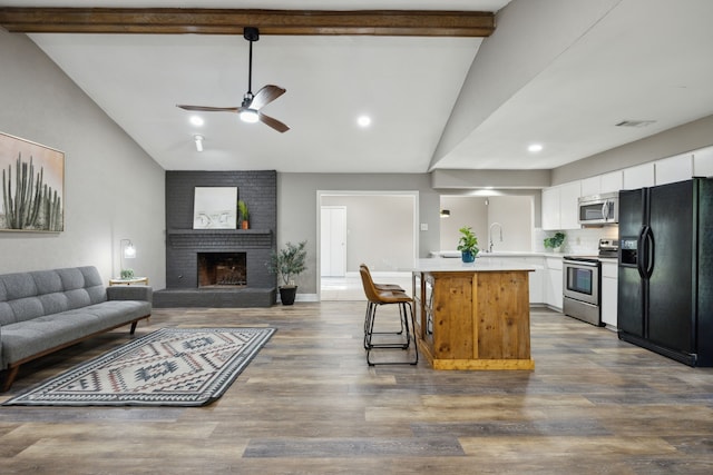 kitchen with open floor plan, light countertops, appliances with stainless steel finishes, white cabinetry, and vaulted ceiling with beams