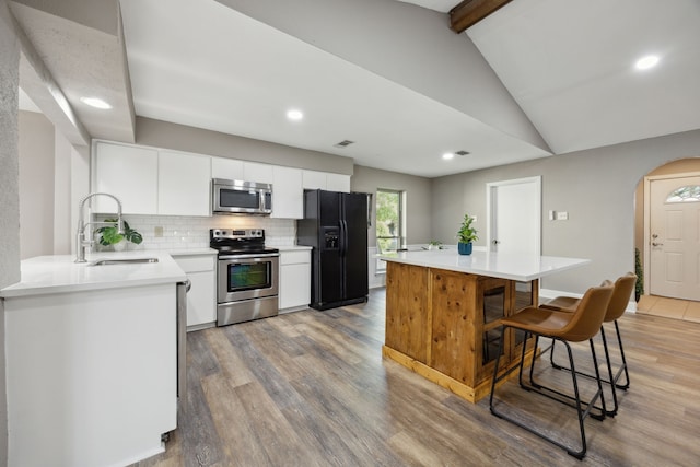 kitchen with lofted ceiling with beams, arched walkways, appliances with stainless steel finishes, a sink, and backsplash