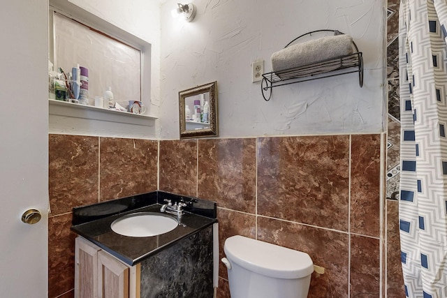 bathroom featuring tile walls, wainscoting, vanity, and toilet