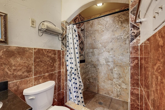 full bath featuring wainscoting, toilet, tile walls, and a stall shower