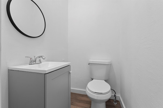 bathroom with toilet, vanity, wood finished floors, and baseboards