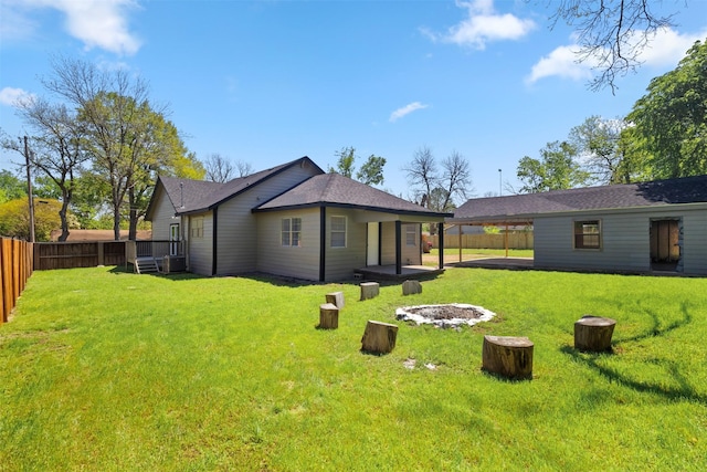 rear view of property featuring a yard, a carport, fence, and an outdoor fire pit