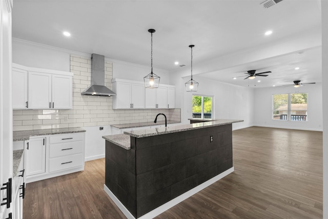 kitchen featuring wall chimney range hood, white cabinets, light stone counters, dark wood-style flooring, and decorative backsplash