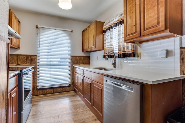 kitchen with a sink, appliances with stainless steel finishes, under cabinet range hood, brown cabinets, and light wood-style flooring