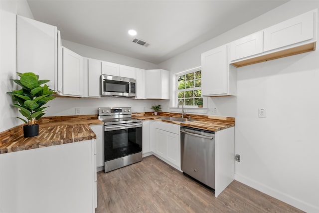 kitchen featuring butcher block countertops, a sink, light wood-style floors, stainless steel appliances, and visible vents