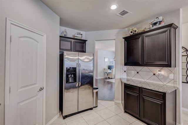 714 Lone Star Ct, Wylie, TX 75098 - kitchen featuring stainless steel refrigerator with ice dispenser, dark brown cabinetry, decorative backsplash, light tile patterned flooring, and light stone counters