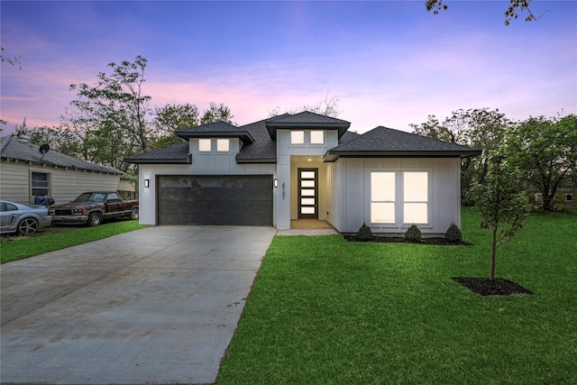prairie-style home featuring a yard, an attached garage, a shingled roof, and driveway