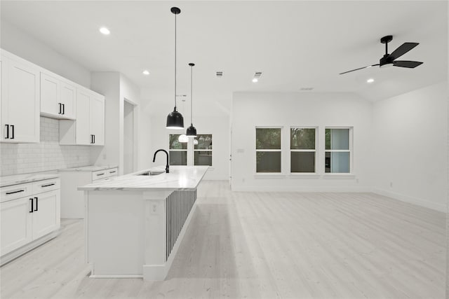 kitchen featuring light wood finished floors, light stone counters, decorative backsplash, and a sink