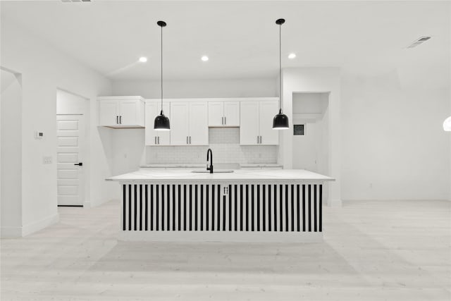 kitchen featuring visible vents, white cabinets, light countertops, a center island with sink, and decorative backsplash