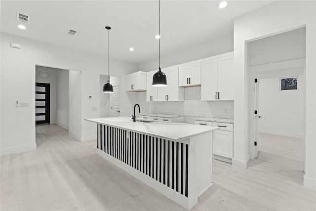 kitchen with tasteful backsplash, visible vents, a sink, a kitchen island with sink, and white cabinetry