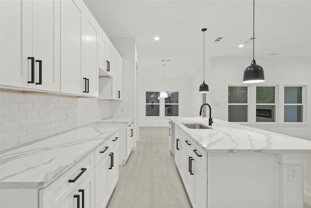 kitchen featuring visible vents, a sink, light wood finished floors, a center island with sink, and backsplash