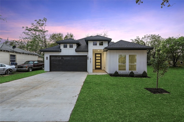 prairie-style home featuring board and batten siding, a front yard, an attached garage, a shingled roof, and driveway