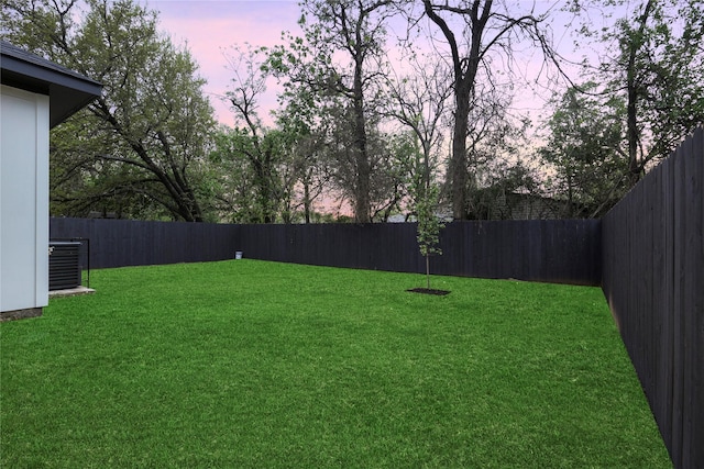 yard at dusk featuring a fenced backyard and cooling unit