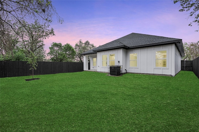 rear view of house featuring a shingled roof, a fenced backyard, central AC, and a lawn