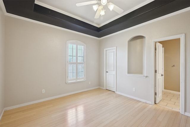 empty room featuring crown molding, ceiling fan, a tray ceiling, wood finished floors, and baseboards