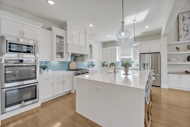 kitchen featuring appliances with stainless steel finishes, a sink, light wood-style flooring, light countertops, and white cabinetry