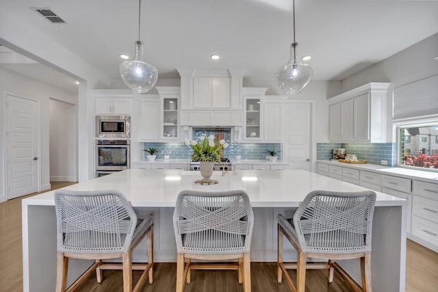 kitchen with appliances with stainless steel finishes, a center island, white cabinetry, light countertops, and decorative backsplash