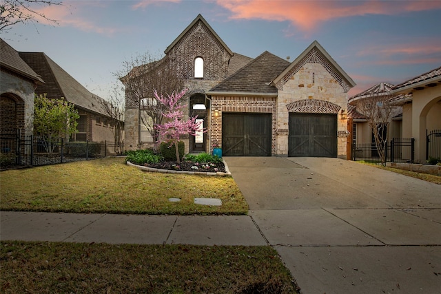 french provincial home featuring concrete driveway, stone siding, an attached garage, brick siding, and fence