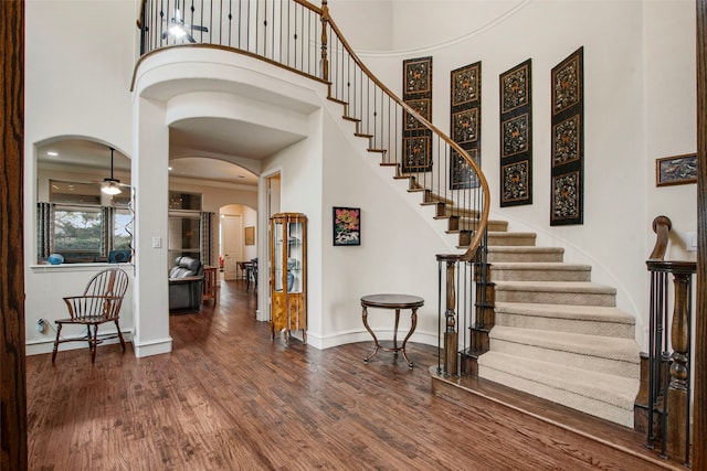 foyer entrance featuring arched walkways, wood finished floors, a high ceiling, stairs, and baseboards