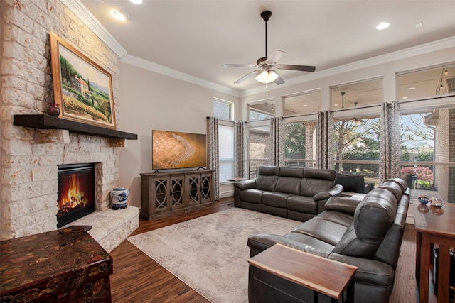 living area featuring ornamental molding, a stone fireplace, a ceiling fan, and wood finished floors