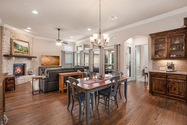 dining area with dark wood-style flooring, arched walkways, crown molding, and a fireplace