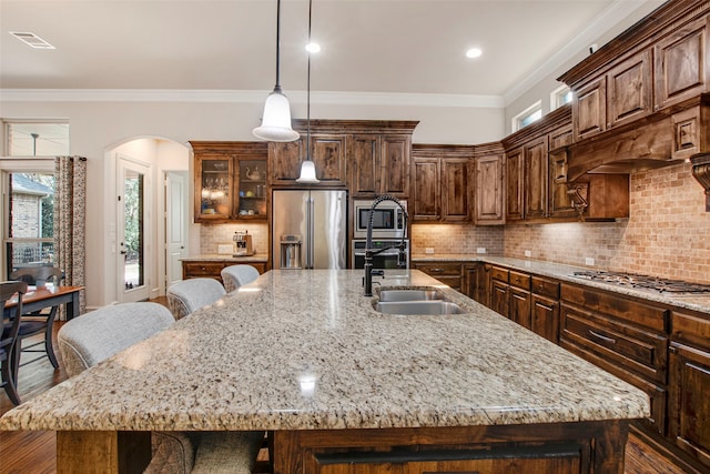 kitchen with ornamental molding, a spacious island, stainless steel appliances, arched walkways, and a sink